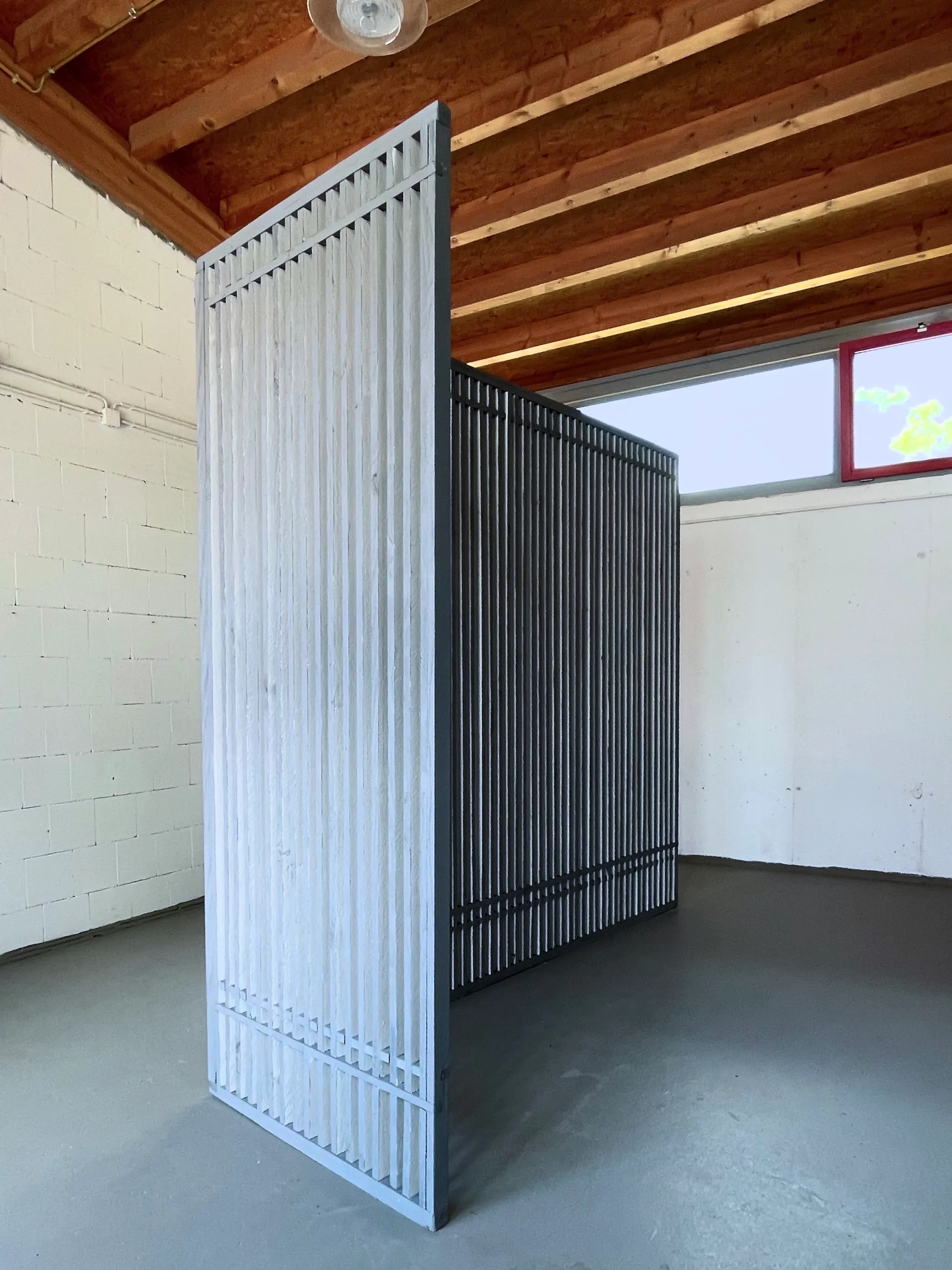 Rear view of the sculptural wall showing vertical wooden slats with alternating black and white side surfaces. The perspective emphasizes the shift in visual density depending on the viewing angle.